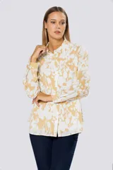Blusa de manga larga con cuello camisero y cierre frontal de botones. Presenta un diseño estampado en tonos beige y blanco.