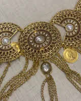 Cinto de metal dorado con diseño de placas circulares con detalles grabados, perlas sintéticas y múltiples cadenas colgantes decorativas.