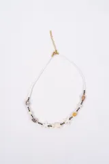 Collar de estilo playero compuesto por pequeñas cuentas blancas, intercaladas con cuentas turquesas y doradas. Presenta dijes de caracoles, estrellas de mar y una tortuga marina en el centro.