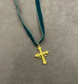 Collar tipo choker de cinta de terciopelo verde con dije de cruz dorada con detalles grabados y letras.