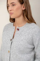 Cardigan de punto color crema con cuello redondo, manga larga y cierre frontal con botones forrados de distintos colores.