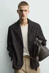 Blazer de corte relajado confeccionada en piel con acabado de ante. Presenta cuello con solapas de muesca, cierre frontal de dos botones, mangas largas y bolsillos de plastrón en la parte delantera. Destaca por sus costuras con efecto lavado que le otorgan un aspecto vintage.