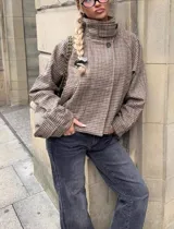 Chaqueta de corte oversize con cuello alto y cierre frontal con botones. Presenta un diseño estampado pied de poule en tonos marrones y beige, con mangas amplias y largo levemente cropped.