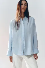 Camisa color coral confeccionada en lino 100%, de corte recto, con cuello solapa, manga larga con puños abotonados y cierre frontal con botones.