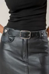 Cinto de cuero color negro con efecto gastado, hebilla metálica rectangular plateada y detalles de tachas metálicas y brillantes en los extremos.