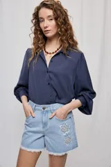 Camisa de manga larga color beige con cuello clásico y botonadura frontal. Presenta mangas con volumen sutil, puños abotonados y una silueta amplia de caída fluida.