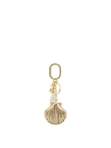 Llavero y colgante para bolso de metal dorado con diseño de concha marina y detalle de piedra transparente.