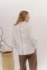 Camisa de manga larga color celeste claro, con cuello camisero y botones frontales. Presenta un detalle de cinta negra alrededor del puño doblado.