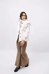 Campera de pana color blanco, de corte oversize, con cuello alto, cierre frontal de botones y volados decorativos en los hombros y cuello.