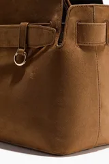 Bolso tote de acabado suave, color marrón, con asas tubulares unidas por una trabilla con hebilla metálica. Presenta una correa decorativa frontal con hebilla metálica y compartimento interior con cierre.