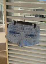 Micro short de jean tiro bajo color celeste claro, con bolsillos traseros tipo cargo con solapa y botón metálico.