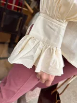 Camisa de manga larga color marfil, con volados en el cuello, en la parte frontal y en los puños, además de mangas abullonadas y puños elásticos fruncidos.