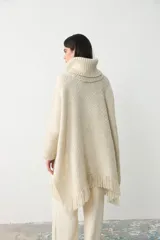Poncho de tejido artesanal en color crudo, con cuello alto tipo polera, mangas largas y terminaciones con flecos en el ruedo.