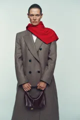 Bolso de mano tipo saca, color borgoña, con asa de mano ajustable y correa bandolera extraíble. Presenta un detalle de doble tira con terminaciones de bolas metálicas doradas en el frente.