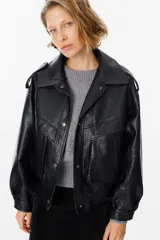 Chaqueta de cuero sintético con textura granulada, corte oversize, cuello camisero, cierre frontal con botones a presión, bolsillos frontales tipo cargo y detalles de charreteras en los hombros.