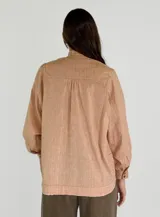 Camisa color beige con cuello mao, mangas largas abullonadas y cierre frontal con botones.