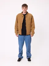 Campera de lona color tostado con cierre frontal, cuello camisero y bolsillo en el pecho. Presenta un diseño de estilo workwear con interior forrado.