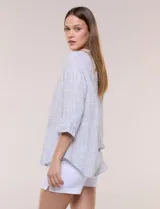 Blusa de silueta relajada con textura tramada, color azul con rayas verticales en tonos rosados, celestes y amarillos. Cuenta con cuello mao abierto en V y mangas tres cuartos amplias con pequeña abertura lateral en el puño.