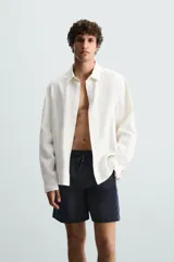 Bañador largo negro con cintura elástica ajustable mediante cordón. Presenta un panel lateral con estampado de cuadros en tonos azul y negro. Incluye bolsillos frontales y un bolsillo trasero con solapa.