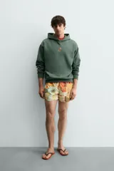 Sudadera con capucha de corte relajado, color verde oscuro, con interior perchado y bordado pequeño de una silla en el centro del pecho.