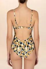 Traje de baño entero con estampado de hojas en tonos mostaza, negro y blanco. Presenta escote corazón con detalle de adorno metálico dorado con forma de hoja en el centro del busto. Tiene tirantes finos ajustables.