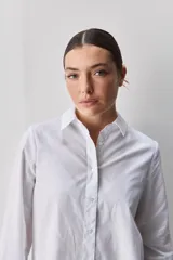 Camisa de algodón blanca, de calce relajado, con cuello clásico, mangas largas y cierre frontal con botones.