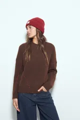 Sweater de tejido suave color marrón con diseño de líneas bordadas en color rojo. Presenta cuello redondo, manga larga y calce relajado.