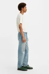 Jean de corte relajado y pierna cónica, con diseño de cinco bolsillos y cierre frontal con botones. Presenta un lavado azul claro con efecto desgastado, roturas localizadas y detalles de salpicaduras de pintura.