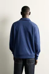 Sudadera polo de corte regular, confeccionada en tejido técnico interlock de algodón con elasticidad. Presenta cuello solapa, cierre frontal de cremallera y manga larga con puños acabados en rib.