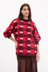 Sweater de punto con diseño geométrico de cuadros en tonos bordó, rojo y rosa. Presenta cuello redondo, mangas largas con puños ajustados y un corte holgado.