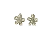 Par de aros tipo botón con diseño de flor de cinco pétalos en metal plateado texturizado con acabado brillante.