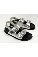 Sandalias negras de charol estilo flatform, con dos tiras frontales con hebillas metálicas grandes y ojales decorativos, y tira trasera con hebilla ajustable.