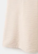 Vestido corto de color beige con diseño fluido, tejido plisado, cuello redondo y tirantes finos ajustables.