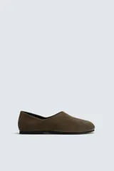 Zapato tipo mocasín sin cordones fabricado en piel con acabado serraje. Presenta talón plegable, horma redonda y suela de goma Vibram.