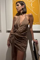 Vestido corto de gasa tornasol color cobre, con escote pronunciado en V, cuello halter y espalda baja. Presenta un diseño drapeado en la cadera con un lazo largo ajustable que permite múltiples usos.