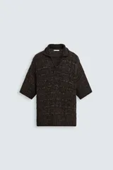 Polo de punto de calce relajado, color marrón oscuro jaspeado con negro. Presenta cuello solapa con abertura frontal en V y mangas cortas.