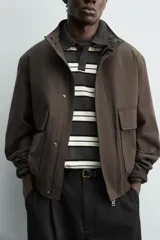 Cazadora regular fit de tejido técnico color marrón, con cuello subido, bolsillos de plastrón con solapa en la cadera, mangas largas con puños elásticos y cierre frontal con cremallera oculta por solapa con botones a presión.