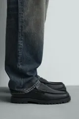Mocasín de vestir negro, estilo penny loafer con antifaz en el empeine. Presenta forro y plantilla interior a tono, y suela track gruesa y dentada.