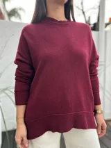 Sweater de punto color bordó, con cuello redondo y diseño holgado. Presenta puños y ruedo acanalados, con un corte ligeramente más largo en la parte posterior.
