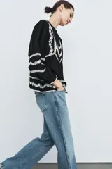 Blusa negra de manga larga con cuello redondo y cierre frontal de botones. Presenta amplios detalles de bordados y encajes blancos en el canesú frontal, mangas y ruedo inferior.