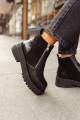 Botas cortas negras con plataforma dentada, confeccionadas en una combinación de cuero con textura de reptil y paneles de gamuza. Presentan un cierre frontal metálico y puntera cuadrada.