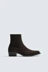 Bota estilo cowboy de caña media, confeccionada en piel con acabado de gamuza en color marrón oscuro. Presenta horma en punta, cierre lateral y suela con tacón cuadrado bajo.