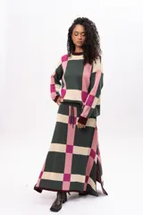 Pollera midi de tejido de punto con diseño geométrico de cuadros en tonos verde, rosa y beige. Presenta cintura elástica con cordón de ajuste y aberturas laterales en el ruedo.