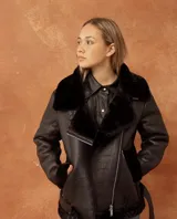 Campera tipo gamulán de cuero vegano negro con interior y cuello de piel sintética al tono. Presenta cierre frontal cruzado y diseño de corte clásico.