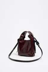 Bolso de hombro Bimba y Lola tamaño mini, de estructura blanda y color marrón oscuro, confeccionado en piel vacuna. Presenta asas de mano de piel y una correa extraíble, con detalles metálicos y logo de la marca en el frente.