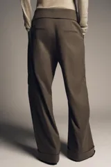Pantalón de tiro medio color marrón oscuro, estilo cargo, con cintura acabada en vuelta asimétrica, pliegues delanteros y bolsillos laterales y con solapa en las piernas.