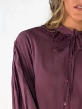 Camisa negra de corte holgado con cuello tipo bebé con volados y lazo de ajuste, cierre frontal con botones y mangas largas abullonadas con puños abotonados.