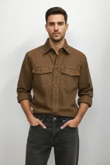 Camisa de jean color marrón, con cuello clásico, cierre frontal de botones y dos bolsillos con solapa en el pecho.