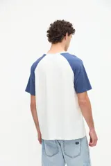 Remera estilo raglán color blanco en el cuerpo con mangas cortas color arena y cuello redondo marrón. Presenta un pequeño bordado en el pecho.