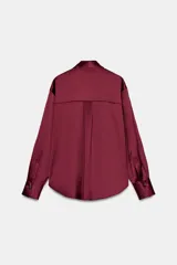 Camisa de cuello solapa y manga larga, confeccionada en tejido satinado con acabado brillante. Presenta cierre frontal con botones y bajo asimétrico.
